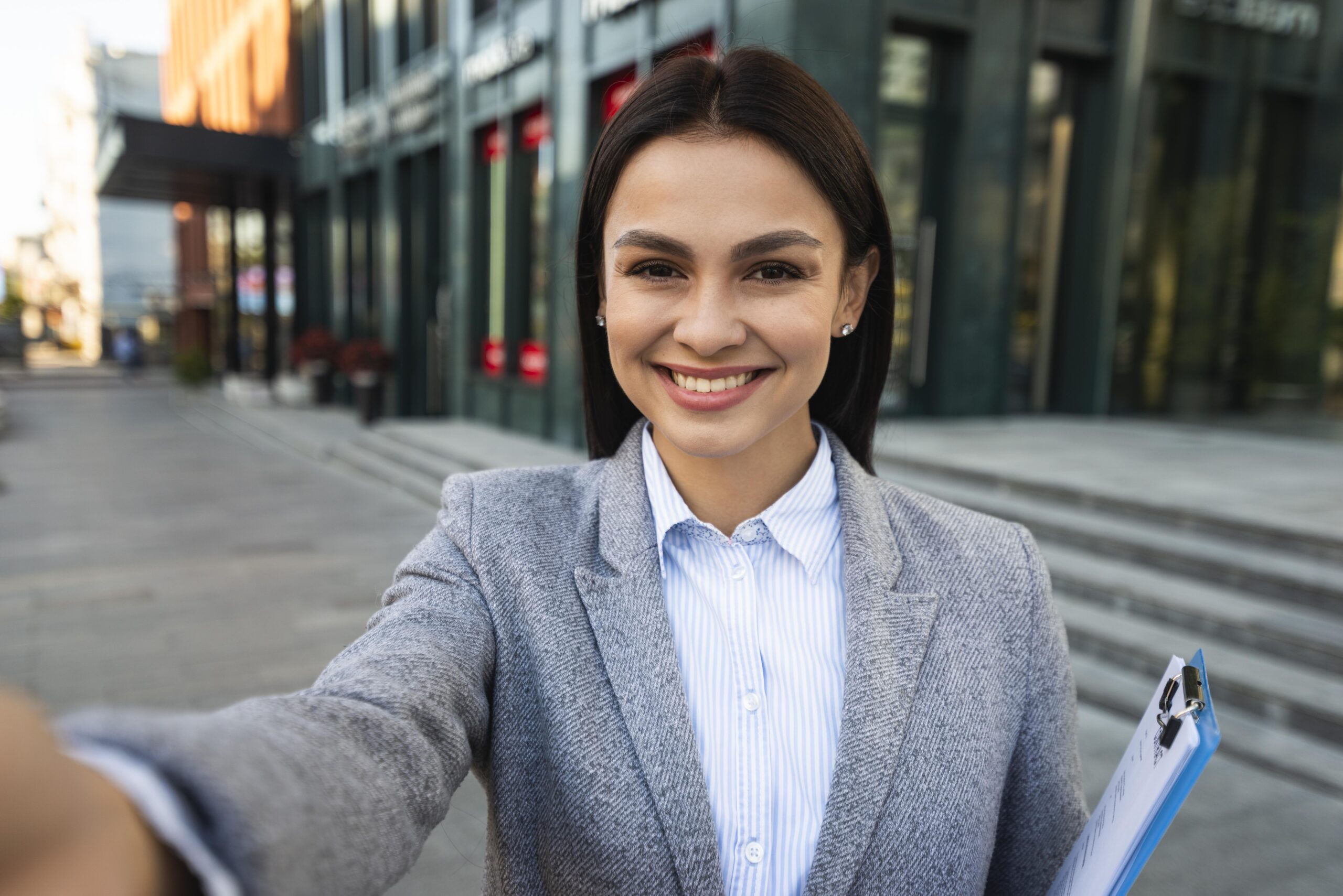 smiley-businesswoman-with-clipboard-taking-selfie-city smiley-businesswoman-with-clipboard-taking-selfie-city